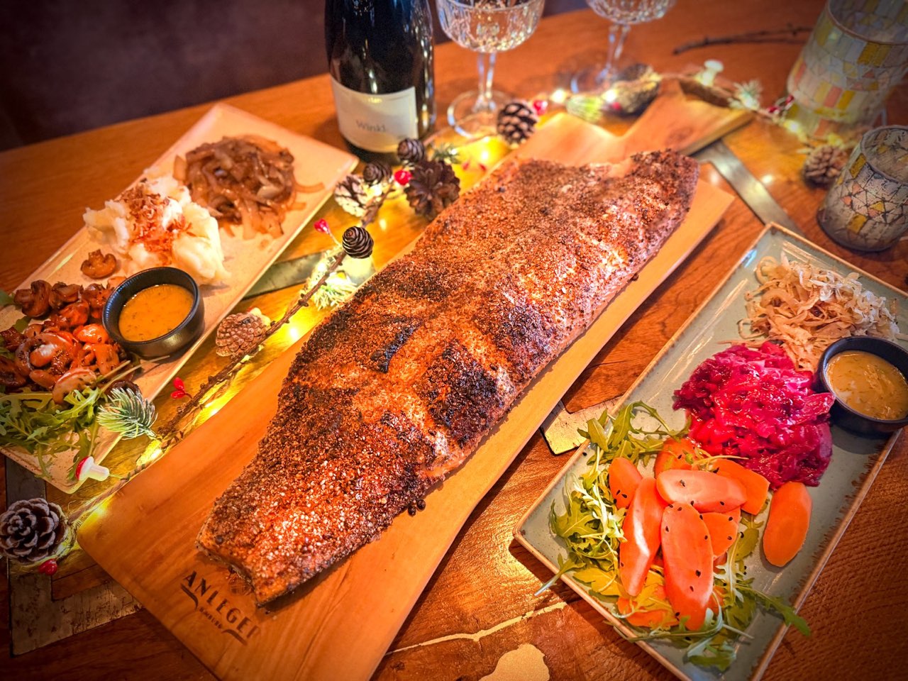 Ganze Seite Flammlachs auf einem Holzbrett mit Beilagen, Lichterkette und Wein auf dem Tisch