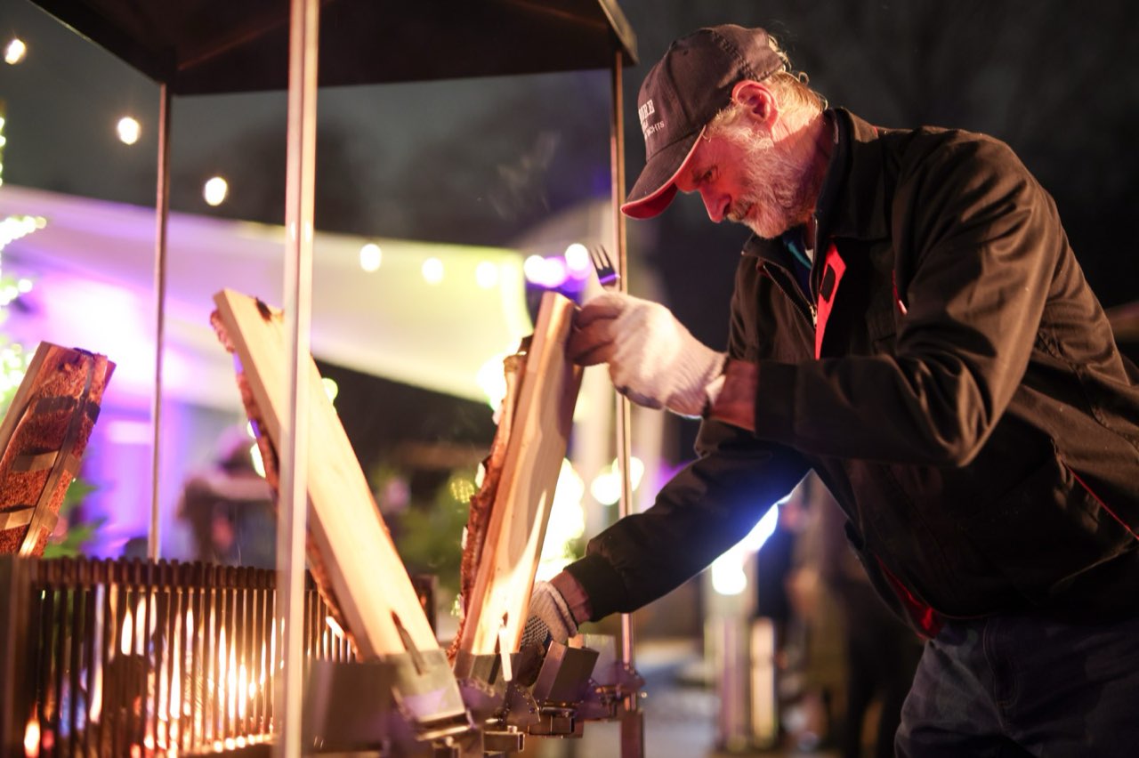 Der Grillmeister stellt ein Brett mit Lachs an das Feuer