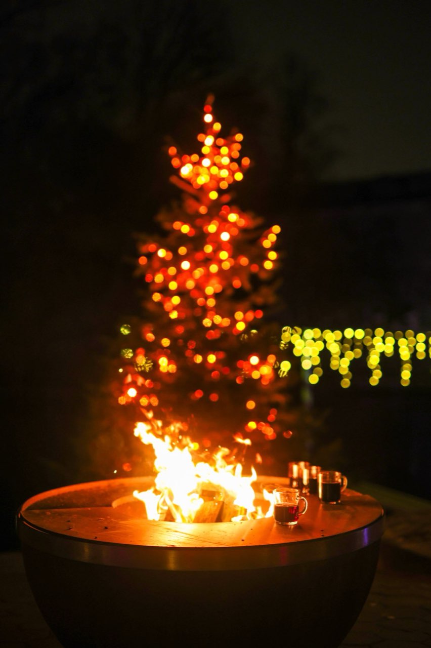 Brennende Feuerschale vor einem rot leuchtenden Tannenbaum
