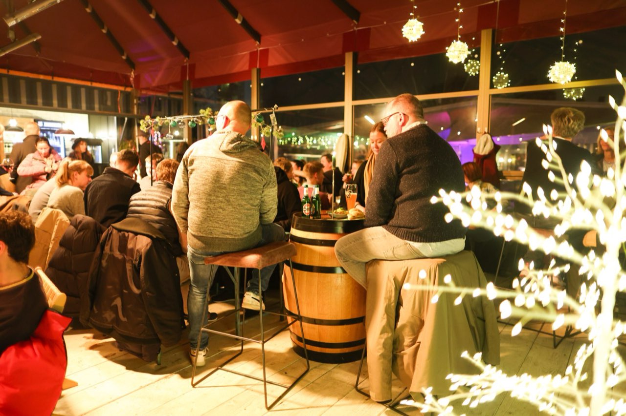 Gut besuchtes Winterzelt, Gäste an Fasstischen unter Lichterketten